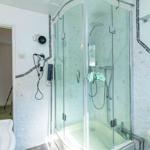 Badezimmer mit Dusche, Toilette und Waschbecken. Wände mit Mosaikfliesen verkleidet.