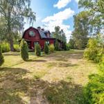 Rotes Haus mit Garten und Bäumen unter blauem Himmel.
