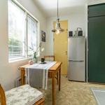 Essbereich mit Holztisch, Stühlen und Kühlschrank. Fenster mit Jalousien und grüner Schrankwand.