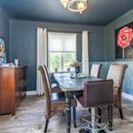 Esszimmer mit Holztisch, Stühlen und Wandbild mit roter Blume.