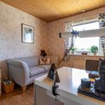 Ein Arbeitszimmer mit Sofa, Schreibtisch und Fenster mit Vorhängen.