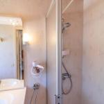 Bad mit Dusche, Waschbecken und Spiegel. Wandverkleidung mit Blattmuster.
