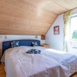 Schlafzimmer mit Holzdecke, Bett und Fenster mit Blick auf Wald.