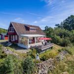 Rotes Haus mit Terrasse und Garten. Roter Sonnenschirm auf der Veranda.