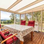 Terrasse mit Tisch, roten Stühlen und Grill. Blick auf Wald und See.