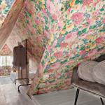 Schlafzimmer mit floraler Tapete, grauer Couch und Kleiderständer.