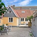 Hinterhof mit Tisch, Stühlen und Terrasse. Haus mit gelbem und grauem Holz. Dach mit roten Ziegeln.