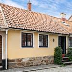 Ein gelbes Haus mit Steinsockel, rotem Ziegeldach und schwarzen Fensterrahmen.