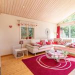 Wohnzimmer mit weißem Sofa, rotem Teppich und Glas-Tisch. Holzdecke und große Fenster.