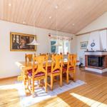 Esszimmer mit Holztisch, Stühlen und Kamin. Holzdecke und -boden. Rote Vorhänge.
