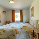 Schlafzimmer mit Bett, Nachttisch und Fenstern mit orangefarbenen Vorhängen.