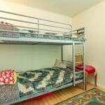 Zimmer mit Doppelstockbett, Holzboden und floraler Gardine.