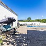 Terrasse mit Pool, Sitzgruppe und Grillplatz. Weiße Mauer und grüne Hecke im Hintergrund.