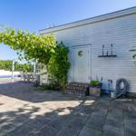Haus mit Terrasse, Pool und Pflanzen. Tür mit Rundfenster und Gartengeräte.