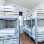 Zwei Etagenbetten mit Matratzen und Bettwäsche in einem Raum mit Holzboden und weißem Holzverkleidung.