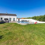 Haus mit Pool, Grillplatz und Trampolin auf grünem Grundstück unter blauem Himmel.