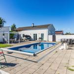 Haus mit Pool, Terrasse und Gartenmöbeln unter blauem Himmel.