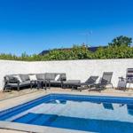 Poolbereich mit Sitzgruppe und Liegestühlen an weißer Wand.
