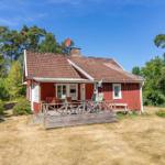 Rotes Holzhaus mit Terrasse, Garten und Wald im Hintergrund.