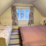 Zimmer mit zwei Betten, Fenster mit Vorhängen und schrägen Wänden.