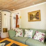 Ein Wohnzimmer mit grünem Sofa, floralen Kissen und einem weißen Ofen.