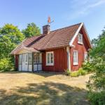 Rotes Holzhaus mit Dach und Antenne, umgeben von Grünflächen und Bäumen.