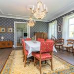 Esszimmer mit Holzboden, gemustertem Teppich und Kronleuchtern. An den Wänden hängen Porträts.