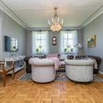 Wohnzimmer mit zwei runden Sesseln, Ledersofa, Holzboden und Kronleuchter.