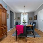 Esszimmer mit Holzboden, Esstisch, Stühlen und Kronleuchter. An der Wand hängen Bilder.