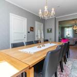 Esszimmer mit Holztisch, schwarzen Stühlen und Kronleuchter. Wohnzimmer im Hintergrund.