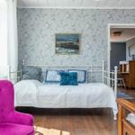 Schlafzimmer mit Bett, pinkem Sessel und floraler Tapete.
