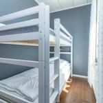 Zimmer mit Doppelstockbett, Holzboden und Fenster mit weißen Vorhängen.