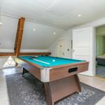 Schlafzimmer mit Bett und Tür. Im Vordergrund befindet sich ein Billardtisch mit grünem Tuch.