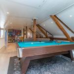 Pooltisch mit blauem Filz in einem Raum mit Holzbalken und Bücherregal im Hintergrund.