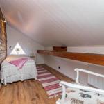 Schlafzimmer mit Holzwand, Bett, Stuhl und Dachschräge.