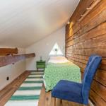 Schlafzimmer mit Holzwand, Bett, Stuhl und Dreiecksfenster unter Dachschräge.