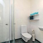 Badezimmer mit Dusche, Toilette und Waschbecken. Weiße Wände und goldener Wasserhahn.