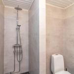 Dusche mit Duschbrause und Toilette in einem Badezimmer mit hellen Wänden.
