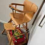 Holz-Hochstuhl mit bunten Perlen und roter Kiste darunter.