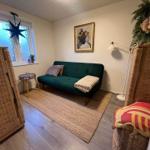 Ein Wohnraum mit grünem Sofa, Teppich und wicker Möbeln. Fenster und Wandbild sind sichtbar.