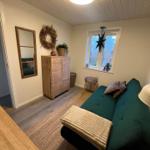 Ein Wohnzimmer mit grünem Sofa, Korbregal und Fenster mit Stern. Holzboden und Wandspiegel.