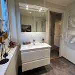 Badezimmer mit Waschbecken, Spiegel und Dusche. Fenster mit Segelboot-Dekoration.