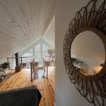 Wohnbereich mit Holzboden, Dachschrägen und Rattan-Spiegel an der Wand.