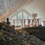 Schlafzimmer mit Blick auf Balkon und Fenster. Holzdecke und Bett mit floraler Bettwäsche.