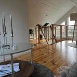 Wohnbereich mit Holzboden, Glas-Tisch und Sitzgelegenheit. Holzgeländer und große Fenster.
