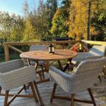 Terrasse mit runden Tisch und vier Stühlen, umgeben von Herbstlaub und Wald.