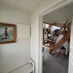 Hausgang mit Bild an der Wand, Blick in Wohnbereich mit Holztreppe und Tisch.