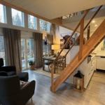 Wohn- und Essbereich mit Küche und Holztreppe. Große Fenster und Türen zu Terrasse.