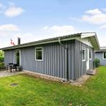 Ein graues Holzhaus mit Garten und Terrasse unter blauem Himmel.
