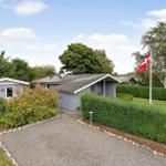 Ein graues Ferienhaus mit Garten, Hecke und dänischer Flagge. 